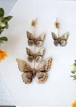گوشواره لنگه به لنگه پروانه آلا با طراحی خاص؛ یک لنگه شامل سه پروانه روی پایه طلایی و لنگه دیگر با پروانه تکی، ساخته شده با استیل و کاور رزین UV
