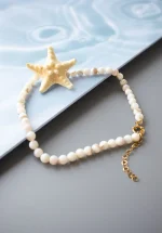 گردنبند ستاره دریایی مدل دریاناز با مرواریدهای سفید و آویز بزرگ ستاره‌ای طلایی، روی سطحی شبیه دریا