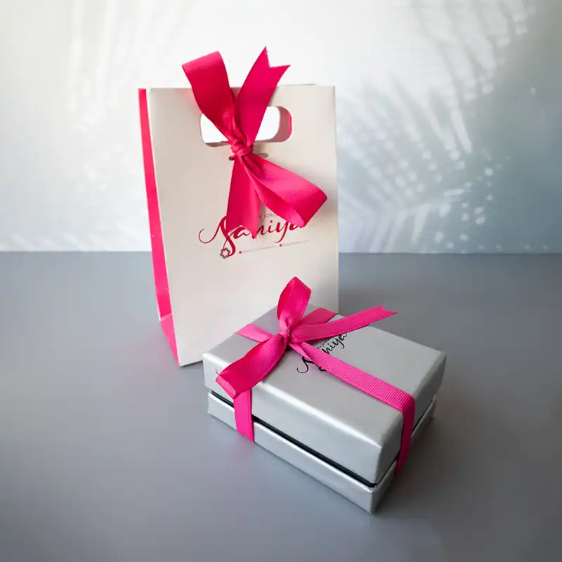 بسته‌بندی لوکس زیورآلات سانیا – جعبه نقره‌ای با روبان سرخابی و پاکت هدیه هماهنگ