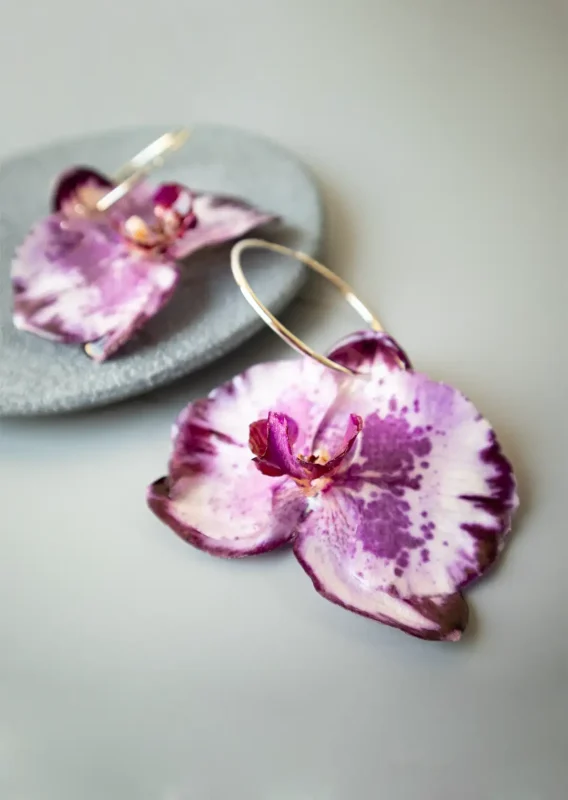 نمای نزدیک از گوشواره حلقه‌ای ارکیده طبیعی مدل آرسینه روی زمینه طوسی